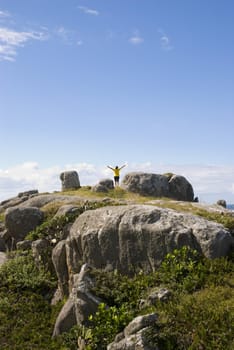 Adult woman photographed from behind with arms open on top of a rocky hill.