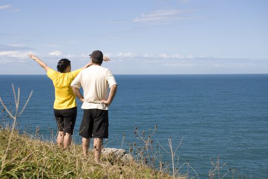 Adult couple in the coastline looking out into the sea, the woman with arms open.