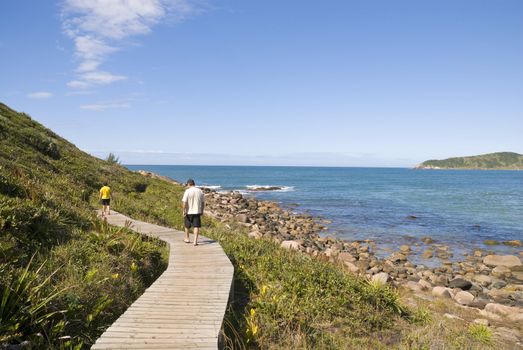 Adult couple hiking in the coastline, walking on a wooden passway.