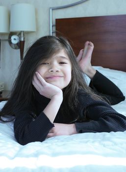 Six year old girl chin on hands thinking while lying down on bed