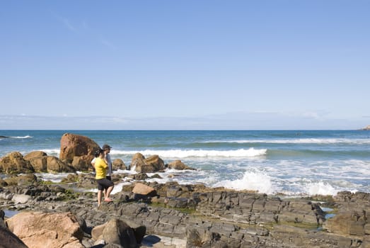 Adult couple in the coastline looking out into the sea, with clear blue sky.