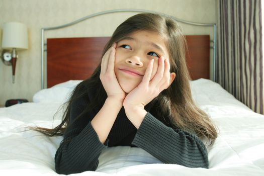 Six year old girl chin on hands thinking while lying down on bed