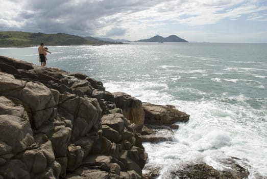 Adult couple standing on a rocky cliff with raging sea beneath.