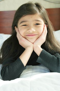 Six year old girl chin on hands thinking while lying down on bed