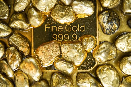 fine gold ingots and nuggets on a wet golden background