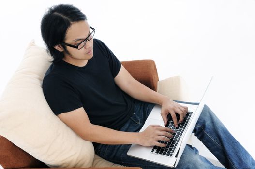 Young Asian man sitting on sofa and using laptop.