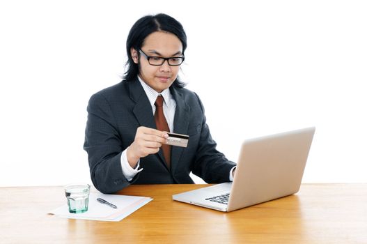 Portrait of a young Asian businessman holding credit card and using laptop over white background.