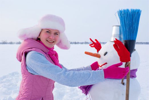 Teenage girl with snowman at winter time