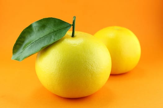Ripe appetizing grapefruit with leaf on orange background.