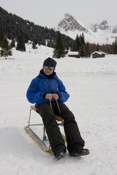 Young boy on a sledge on a snowy trail in val di fassa, in the dolomites