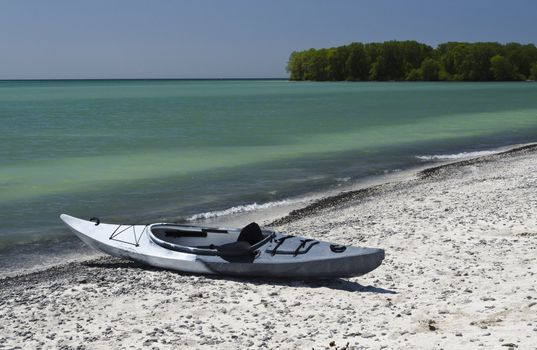 Kayak sitting on the sandy shoreline with deep blue sky and emerald coloured Lake Ontario 