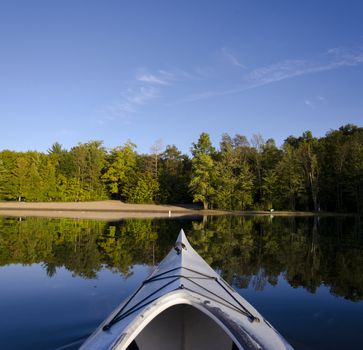 Composite of single kayak resting on calm Charleston Lake facing the beach area with the late day light on the shoreline