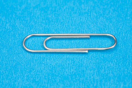 Closeup photo of silver paper clip on blue background.