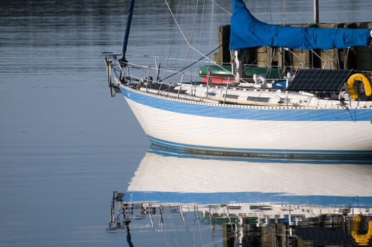 Sailboat reflection docked at a small harbor with morning light