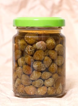 Glass jar with preserved capers on brown paper