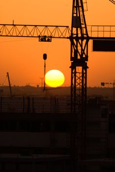 Crane silhouette over sun under construction symbol