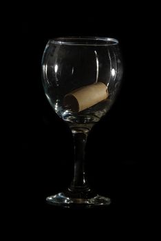 A low key shot of a wine glass with a cork inside.