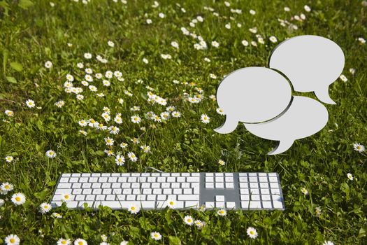 Chat clouds and modern keyboard on green grass in garden