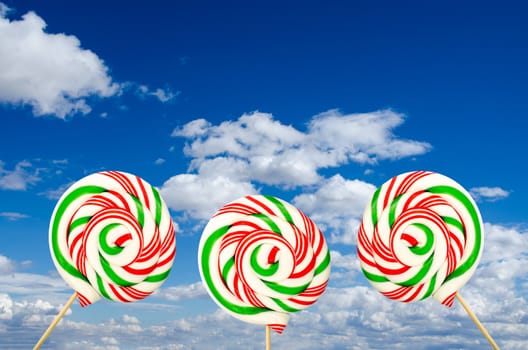 Three sugar lollipops in white green and red on background of sky and clouds