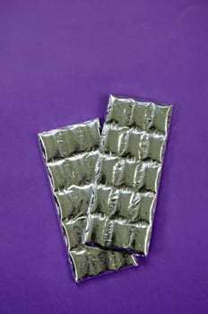 Two foil wrapped chocolate sticks on violet background.