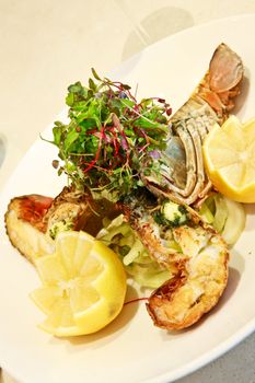 Delicious gourmet grilled lobster or crayfish served topped with a fresh herb salad and lemon on a seafood platter in an upmarket restaurant