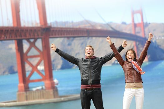 San Francisco happy people tourist couple at Golden Gate Bridge. Young attractive modern couple cheering happy, excited and joyful. California tourism concept with cheerful tourists.