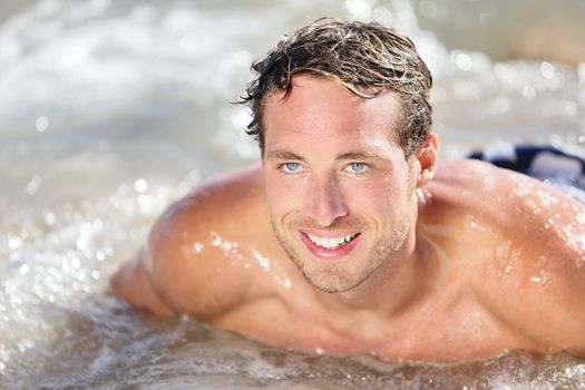 Beach man having fun in water smiling happy. Portrait of young handsome male beach model surfing on bodyboard.