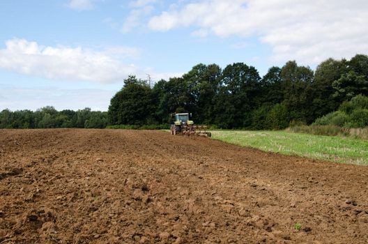 heavy machine tractor plowing agricultural field in end of summer near forest.