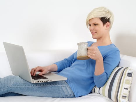 Photo of a beautiful young female sitting on her couch working on a laptop.
