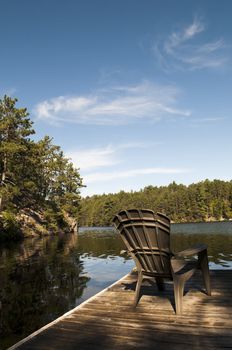 Holiday at the cottage with the sunlight hitting the chair on the dock with lake and shoreline in the background