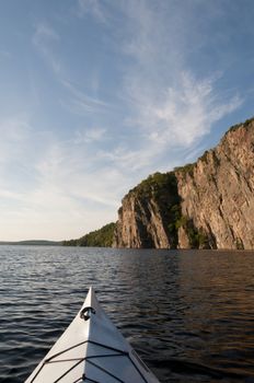 Bow of the kayak in the foreground with the sun drenched Bon Echo cliff is in northern Ontario