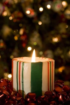 Selective focue on candy striped candle in front of the Christmas Tree with soft focus.