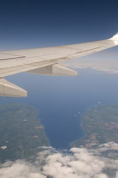 Commercial airplane flying with deep blue sky above and land and clouds below