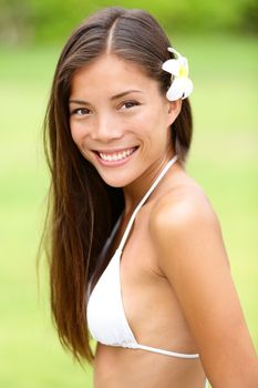 Bikini girl wearing Hawaiian flower in hair. Young woman smiling fresh and healthy. Gorgeous mixed race Asian Caucasian female model on Hawaii.