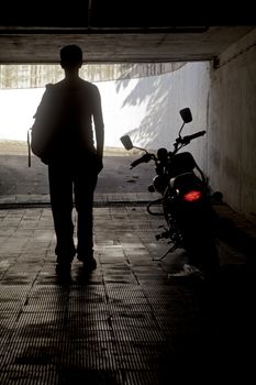 Vertical capture of a man in a white vest with ruck sack back pack stood beside a motor with its tail slights on in a tunnel