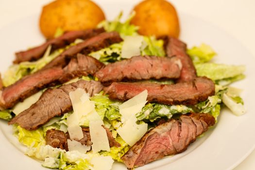 A fresh caesar salad with strips of medium-rare beef and two muffins