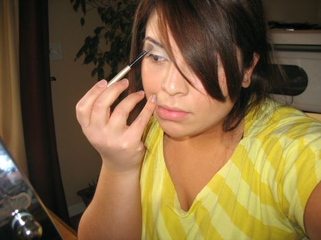A young Spanish woman applying makeup in front of an illuminated cosmetic mirror.