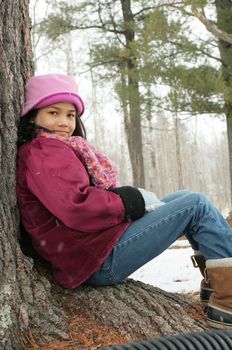 Nine year old girl sitting against tree in winter