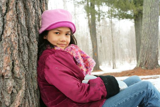 Nine year old girl sitting against tree in winter