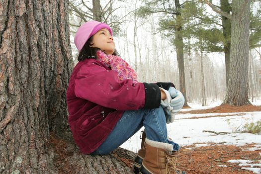 Nine year old girl enjoying sitting under tree in winter