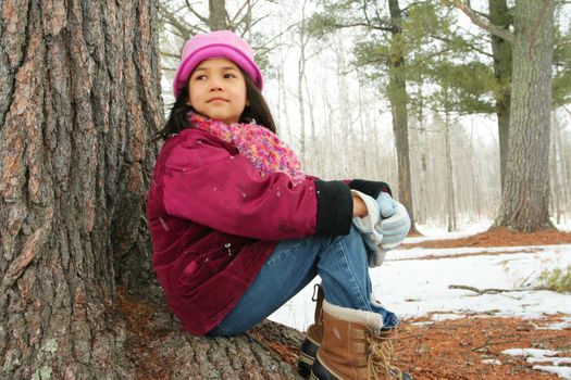 Nine year old girl enjoying sitting under tree in winter