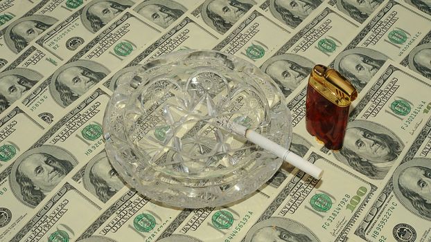 Crystal Ashtray With Cigarette And Lighter On One Hundred Dollar Bills Background.