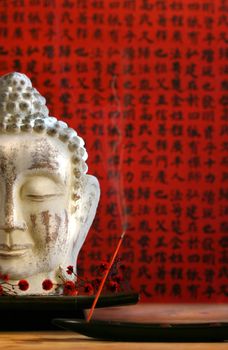 Buddha head and incense against red background