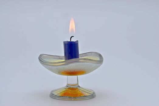 Burning candle in a glass candlestick on a blue background