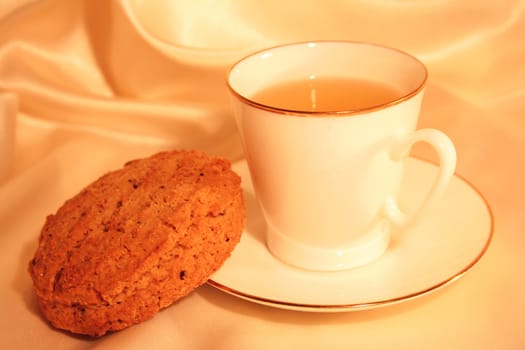 Cup of tea with biscuit on the golden silk background