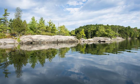 Reflection on a calm lake of a rocky shoreline of a northern lake