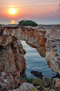 Sunset and stone arch over coastline on Cyprus