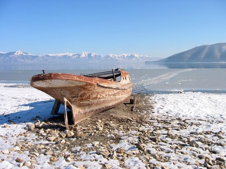 Old lonely boat abandoned at snowy coast,lake prespa, macedonia