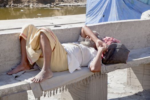 Dwarka Roadtrip. Weary foot traveler takes a rest in the blazing heat of the Indian sun on a bench at Bet Dwarka before he completes his pilgrimage at the Hindu temple in Gujarat India.