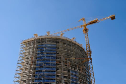 Building crane and building under construction against blue sky